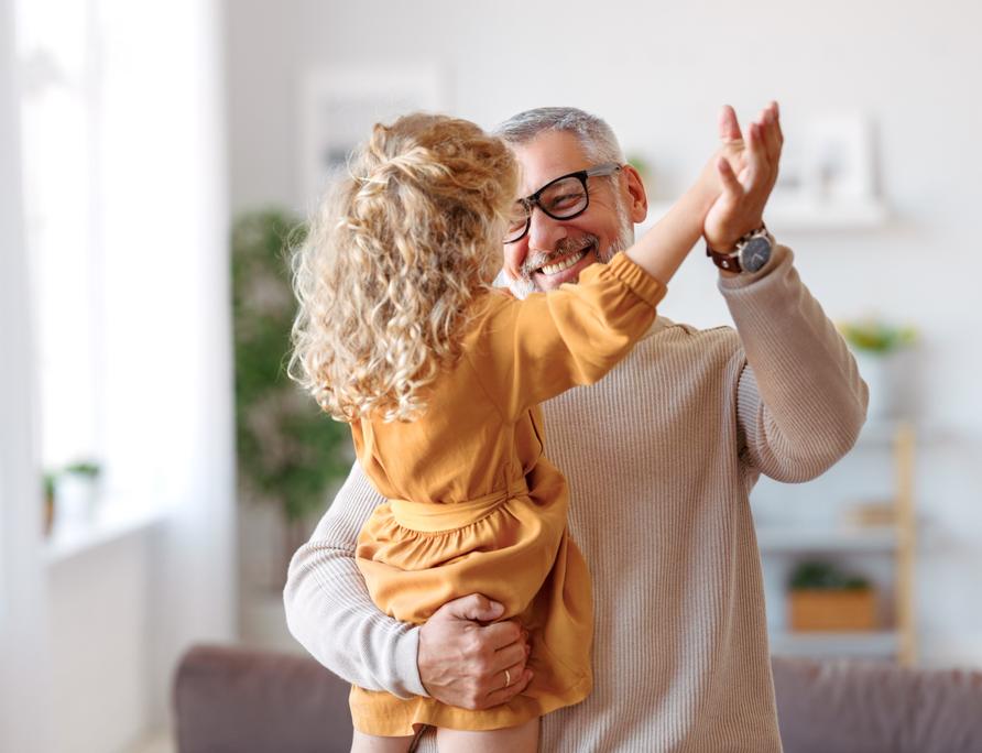 A grandfather playing with his granddaughter at home.
