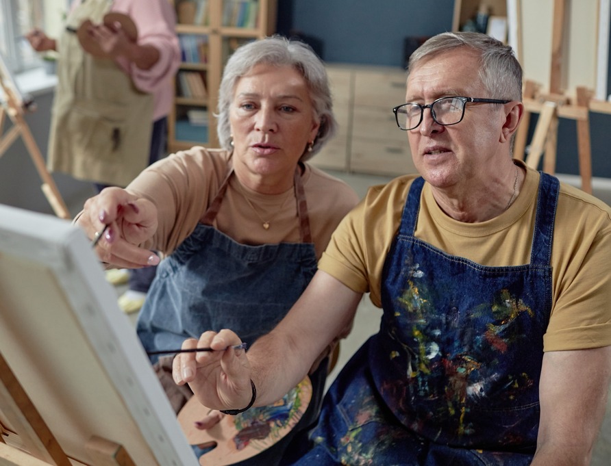 An older couple painting at an easel together.