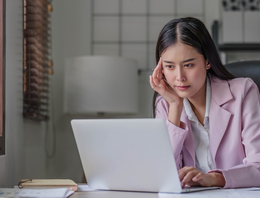 A woman at her computer, thinking carefully.